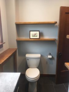 pearl white porcelain toilet in empty bathroom with wooden shelving units