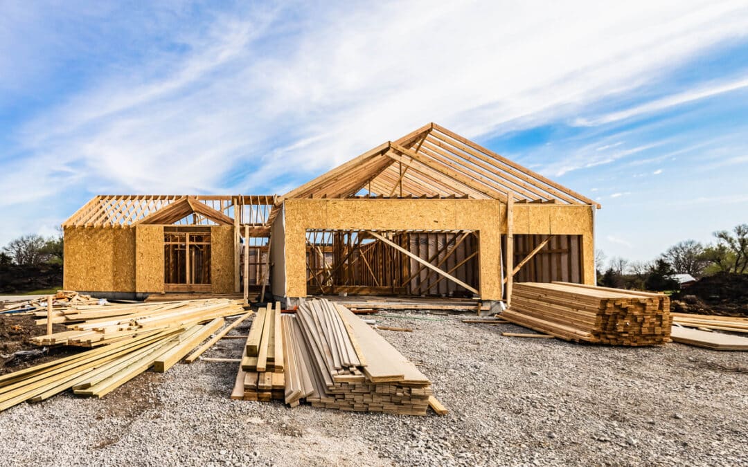 New house under construction, front view from garage door entry with clouds blue sky. Framing of home exterior structure with a pile of lumber and siding plank leftover. Real estate business industry.